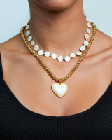 Gold necklace with a heart-shaped pendant worn by a person lean on a neutral background