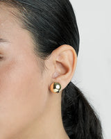 Close-up of a person wearing a gold earring with a blurred background