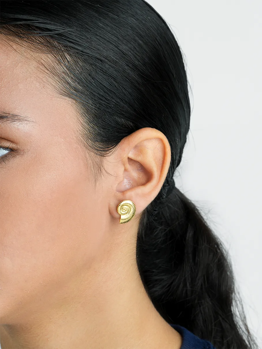 Close-up of a person wearing a gold spiral earring with a plain background