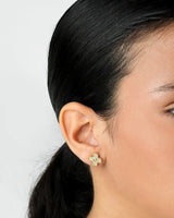 Close-up of an ear wearing a gold earring with green gemstones on a plain background