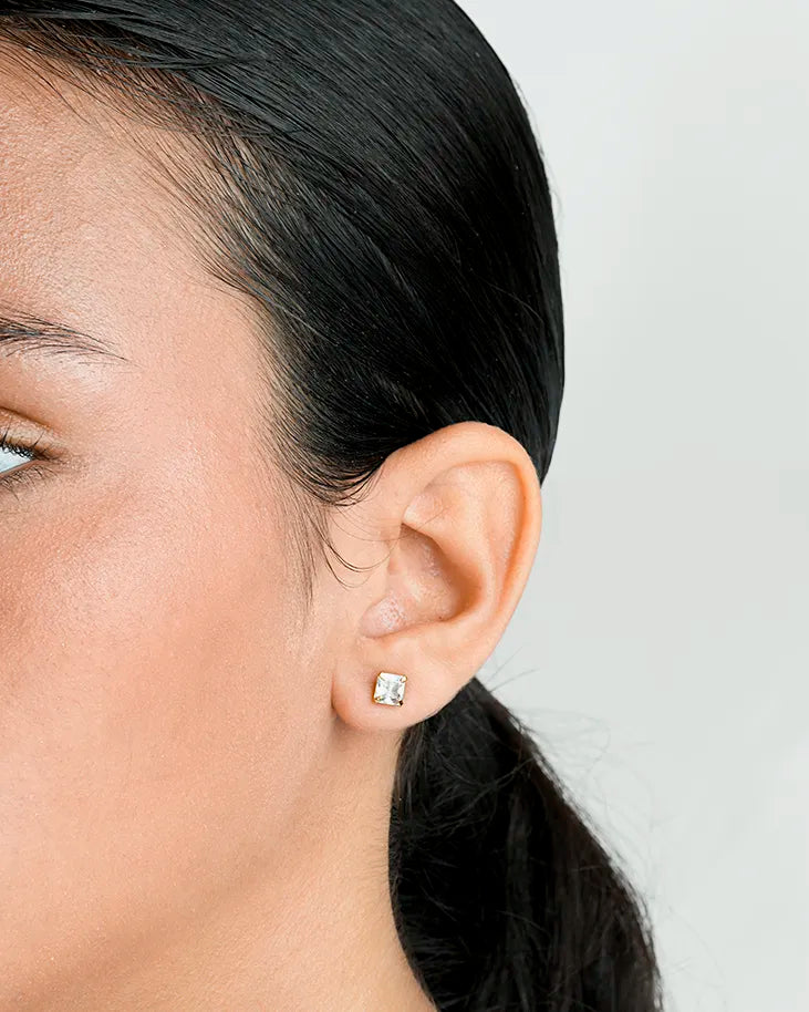 Close-up of a person wearing a diamond stud earring on a plain background