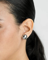 Close-up of an ear wearing a silver stud earring with a blurred background
