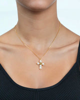 Gold necklace with a cross pendant featuring pearls on a person wearing a black top.