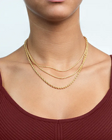 Gold necklaces on a person wearing a maroon top against a light background