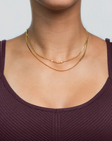 Close-up of a person wearing two gold necklaces with purple shirt