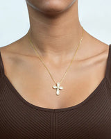 Gold necklace with a leaf pendant worn by a person in a brown top against a neutral background