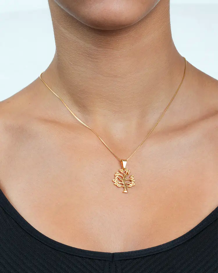 Gold necklace with a tree pendant worn by a person on a plain background