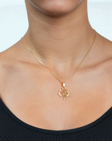 Gold necklace with a tree pendant worn by a person on a plain background