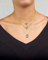 Gold necklaces with green and purple gemstones and a teardrop pendant on a plain background