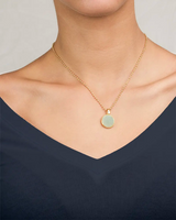 Model wearing Gold necklace with a round green pendant on a person wearing a black top.