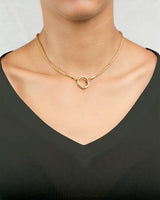 Gold necklace wheat -with a circular pendant on a person wearing a black top.