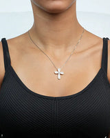 Person wearing a black tank top with a silver necklace featuring a cross pendant.
