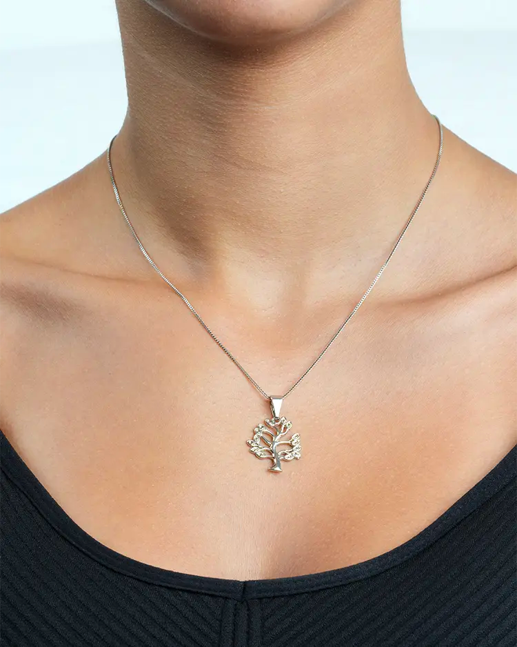 Silver necklace with a tree pendant worn by a person against a neutral background