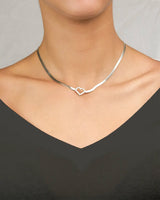 Silver necklace with a heart-shaped pendant worn by a woman against a neutral background